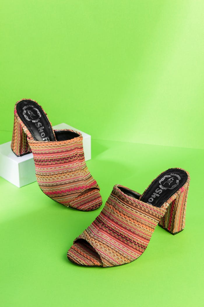 Stylish open-toe heels with colorful stripes on a bright green background - fashion footwear standout.